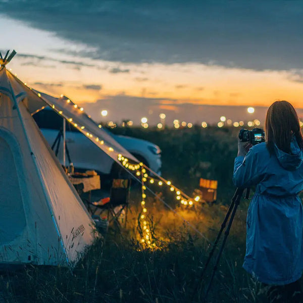 Un campeur photographiant le coucher de soleil avec des guirlandes LED solaires USB autour de sa tente.